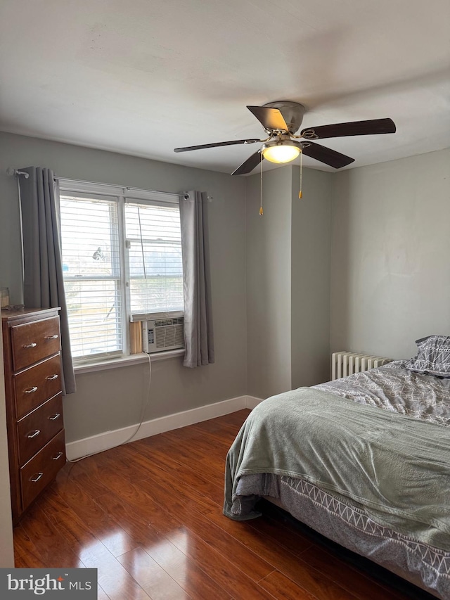 bedroom with wood finished floors, cooling unit, radiator, baseboards, and ceiling fan