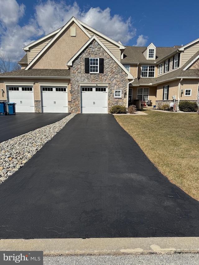 view of front of property featuring a front lawn, a garage, stone siding, and driveway