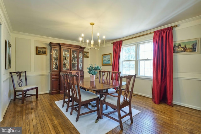 dining space with dark wood-type flooring, a decorative wall, a notable chandelier, and crown molding