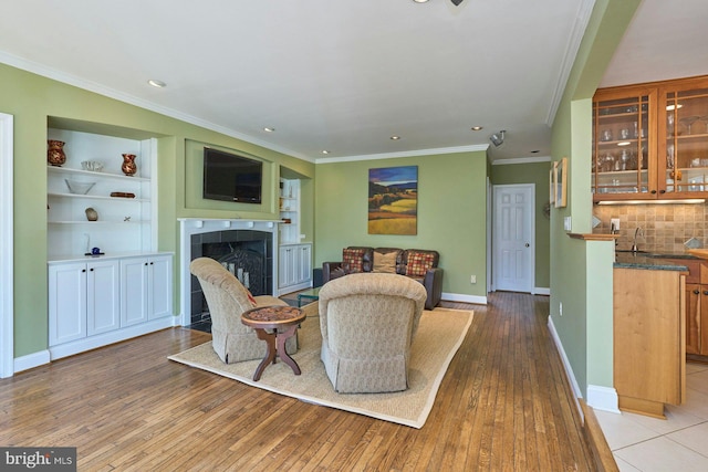 living area featuring built in features, baseboards, ornamental molding, a tile fireplace, and wood-type flooring