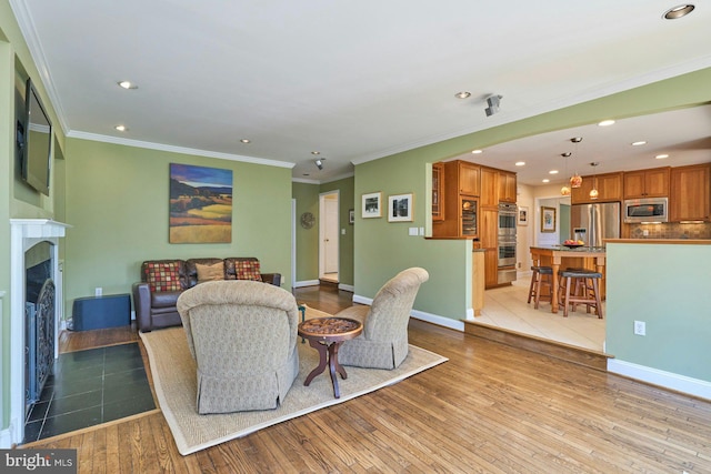 living room with baseboards, a fireplace with flush hearth, recessed lighting, ornamental molding, and light wood-style floors