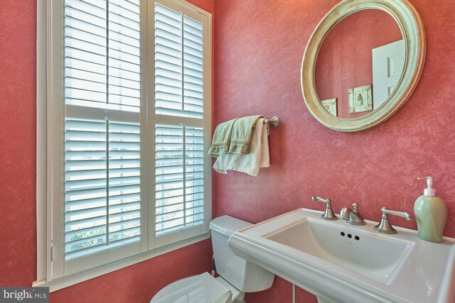 bathroom featuring toilet, wallpapered walls, and a sink