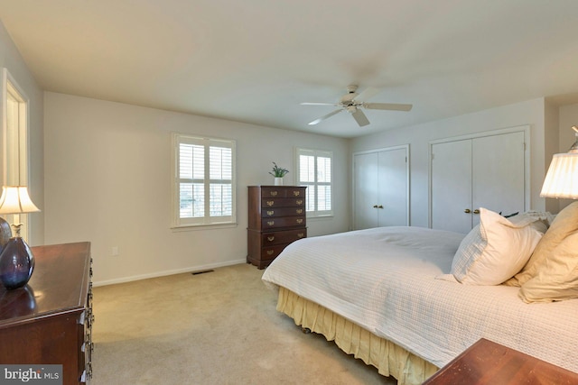 bedroom with a ceiling fan, visible vents, baseboards, multiple closets, and light colored carpet