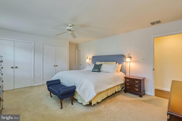 bedroom featuring light colored carpet, visible vents, two closets, and ceiling fan