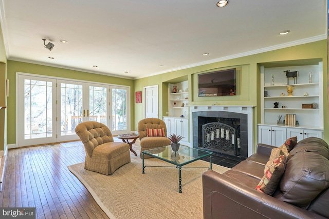 living area featuring built in features, a fireplace, ornamental molding, french doors, and wood-type flooring