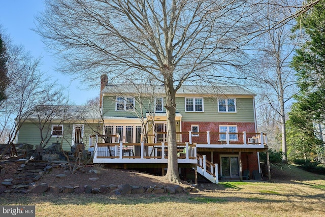 rear view of property featuring a deck, a yard, stairway, brick siding, and a chimney