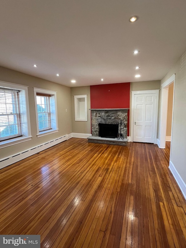 unfurnished living room featuring a baseboard heating unit, recessed lighting, dark wood-type flooring, and a stone fireplace