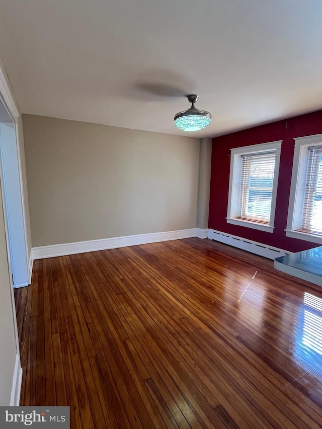 spare room with a baseboard radiator, wood-type flooring, and baseboards