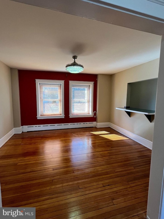 unfurnished living room featuring a baseboard heating unit, baseboards, and wood finished floors