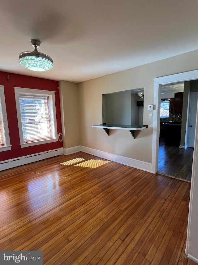 unfurnished living room featuring baseboard heating, baseboards, and hardwood / wood-style floors