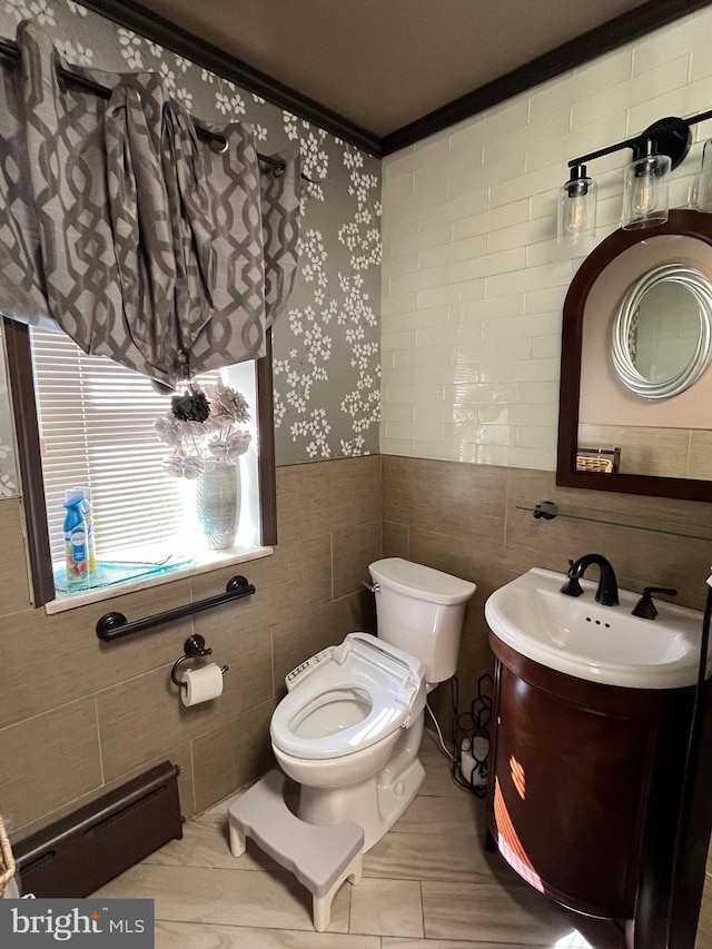 half bath featuring tile walls, toilet, a baseboard heating unit, wainscoting, and vanity