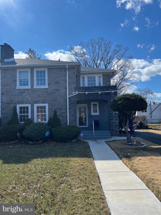 view of front of house with stone siding, a chimney, and a front lawn