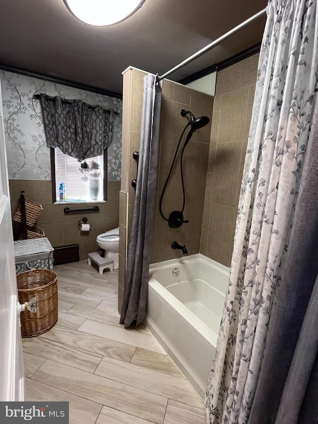 bathroom featuring toilet, a wainscoted wall, tile walls, wallpapered walls, and shower / bathtub combination with curtain