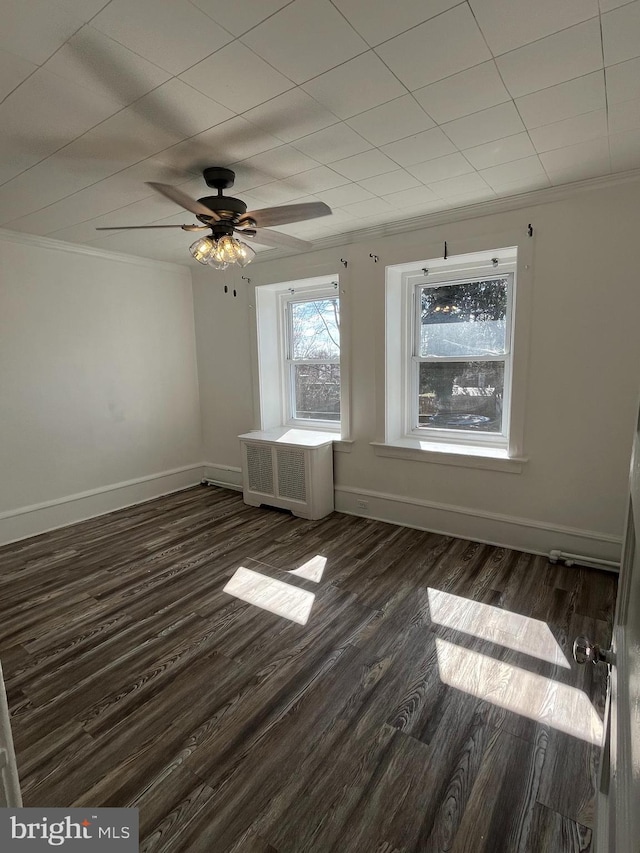 empty room featuring ceiling fan, dark wood-style flooring, baseboards, radiator heating unit, and crown molding