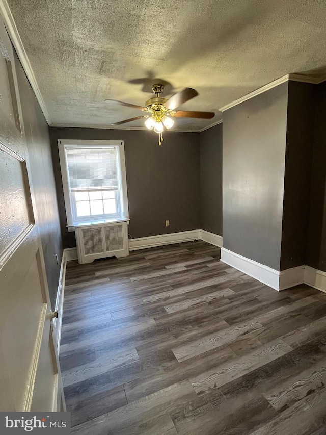 spare room with radiator heating unit, baseboards, dark wood finished floors, and crown molding