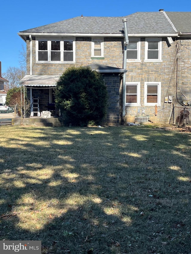 rear view of property with a yard, a shingled roof, and stone siding