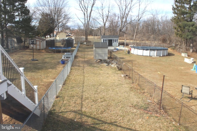 view of yard featuring a fenced in pool, a trampoline, fence, a storage shed, and an outbuilding