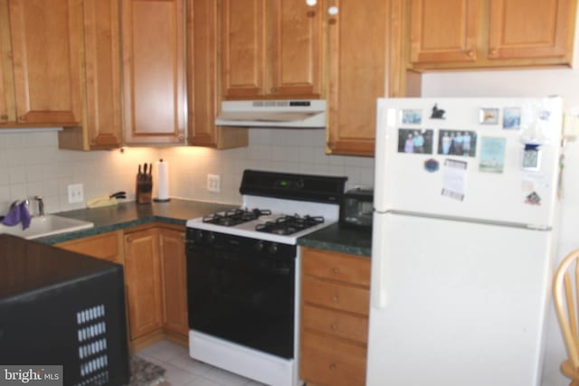 kitchen featuring gas stove, freestanding refrigerator, a sink, under cabinet range hood, and dark countertops