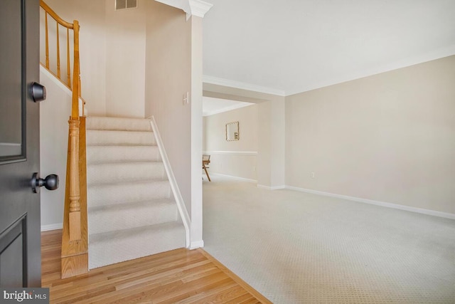 stairway featuring visible vents, baseboards, wood finished floors, and crown molding