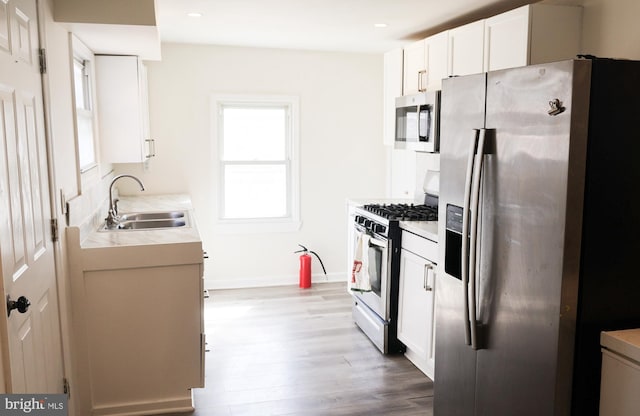 kitchen featuring light wood-type flooring, light countertops, white cabinets, stainless steel appliances, and a sink