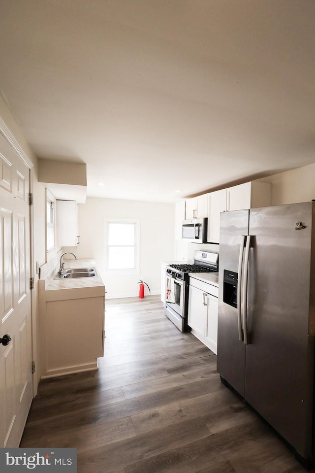 kitchen with light countertops, appliances with stainless steel finishes, dark wood-style floors, white cabinetry, and a sink