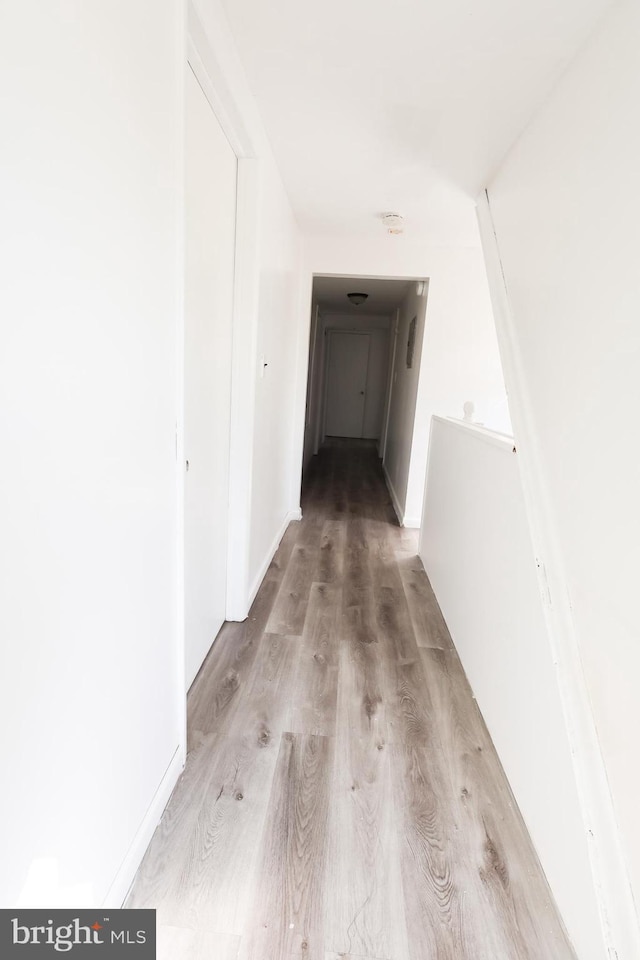 corridor with an upstairs landing, light wood-style floors, and baseboards