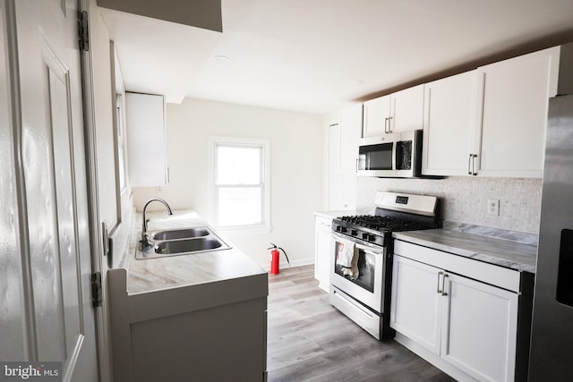 kitchen featuring light wood-style flooring, a sink, decorative backsplash, stainless steel appliances, and white cabinetry