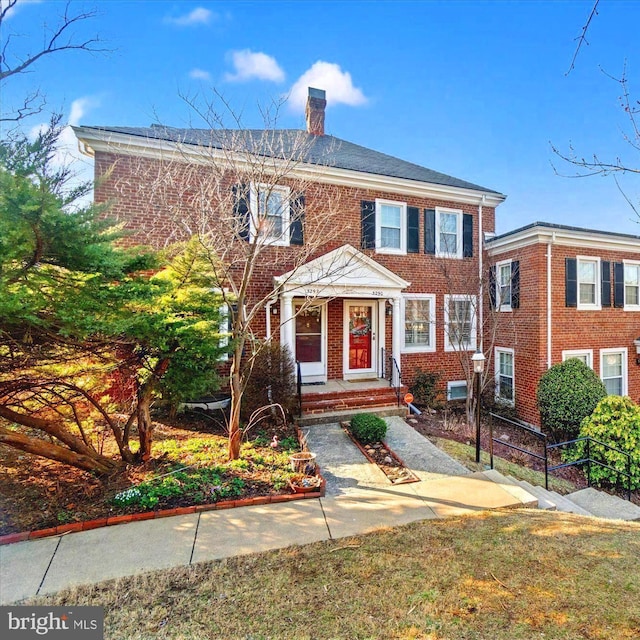 view of front of house with brick siding, a chimney, and fence