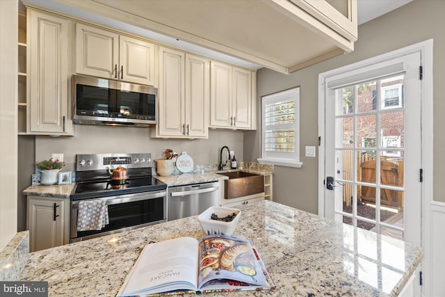 kitchen with light stone countertops, cream cabinets, stainless steel appliances, and a sink