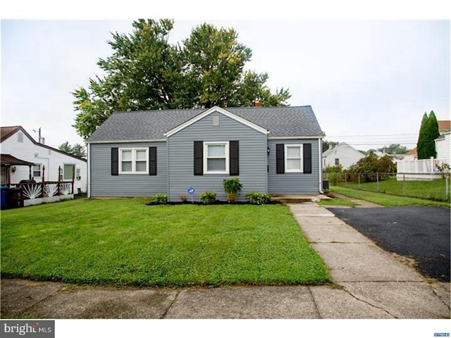 view of front facade featuring a front lawn, fence, roof with shingles, and aphalt driveway