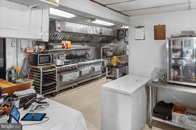 kitchen with light floors, appliances with stainless steel finishes, and concrete block wall