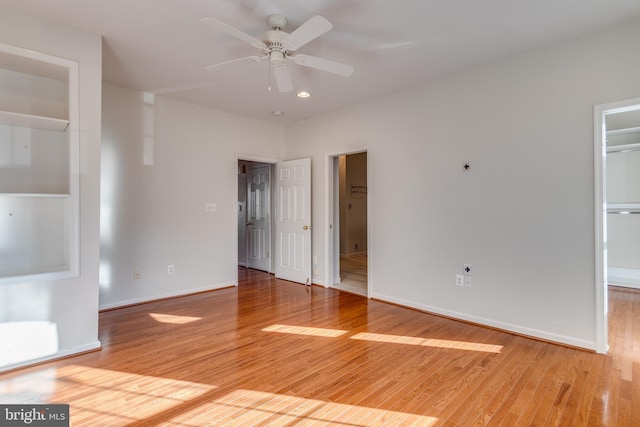 unfurnished bedroom featuring a spacious closet, baseboards, light wood-style flooring, ensuite bathroom, and a closet