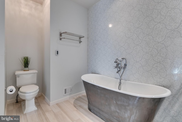 full bathroom featuring wood finished floors, baseboards, visible vents, a freestanding tub, and toilet