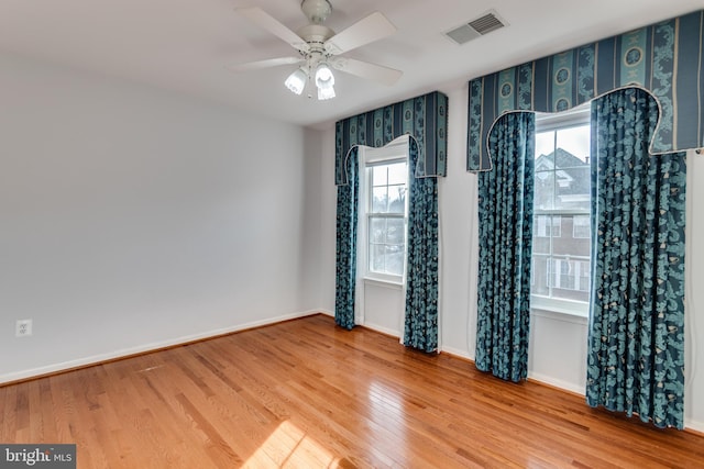 unfurnished room with plenty of natural light, wood finished floors, visible vents, and baseboards