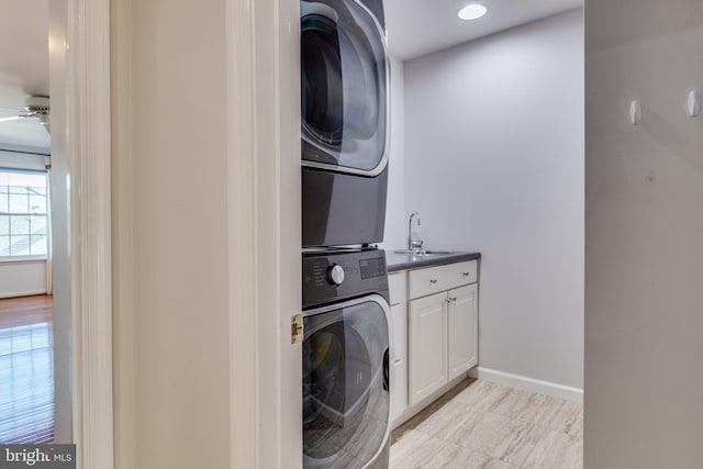 washroom featuring a sink, cabinet space, stacked washer / dryer, baseboards, and ceiling fan