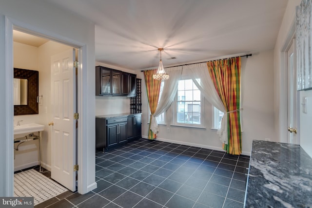 interior space with a chandelier, dark stone countertops, baseboards, and dark tile patterned flooring