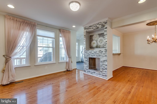 unfurnished living room featuring baseboards, a tile fireplace, ornamental molding, wood finished floors, and a notable chandelier