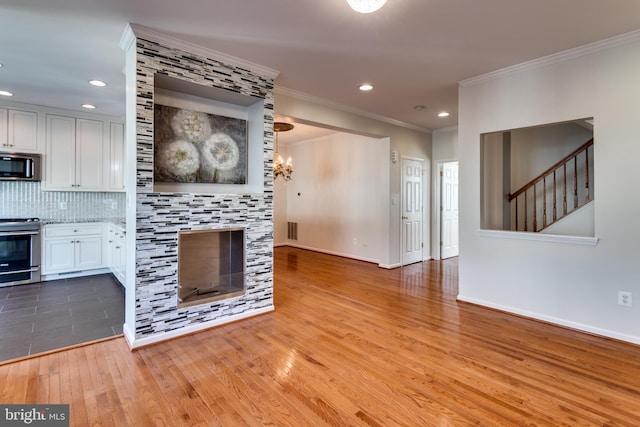 kitchen featuring light wood-style flooring, decorative backsplash, appliances with stainless steel finishes, crown molding, and a chandelier