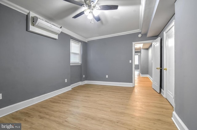 unfurnished room with light wood-style floors, a wall mounted air conditioner, crown molding, and baseboards