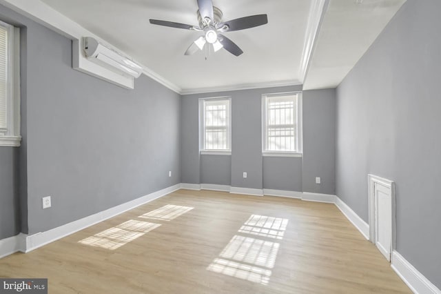 empty room with crown molding, light wood-style flooring, an AC wall unit, ceiling fan, and baseboards