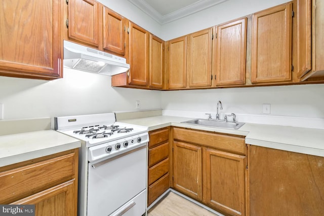 kitchen with white gas range oven, light countertops, crown molding, under cabinet range hood, and a sink