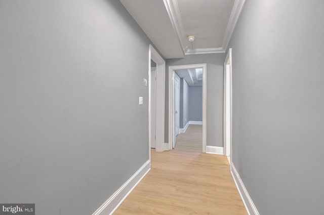 corridor with ornamental molding, light wood-style flooring, and baseboards