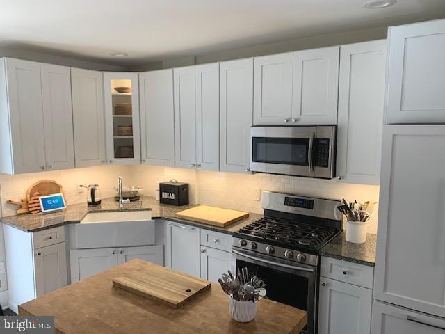 kitchen featuring tasteful backsplash, glass insert cabinets, appliances with stainless steel finishes, white cabinetry, and a sink