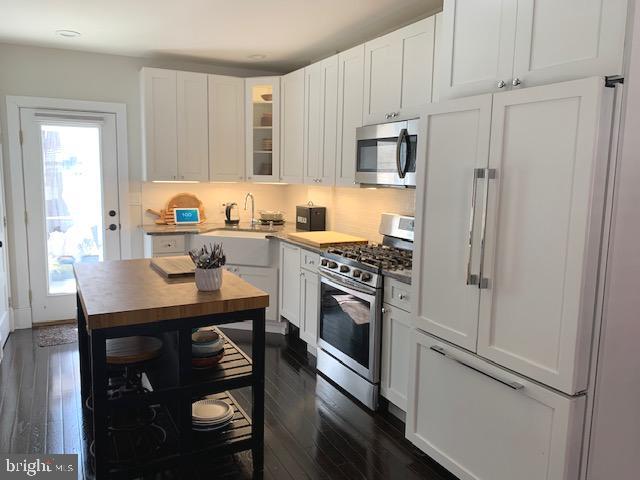 kitchen with a sink, white cabinetry, appliances with stainless steel finishes, glass insert cabinets, and dark wood-style flooring