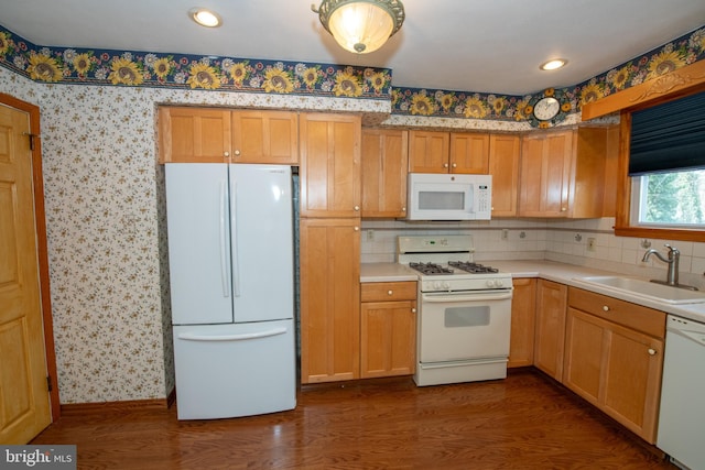 kitchen with a sink, wallpapered walls, white appliances, light countertops, and dark wood-style flooring