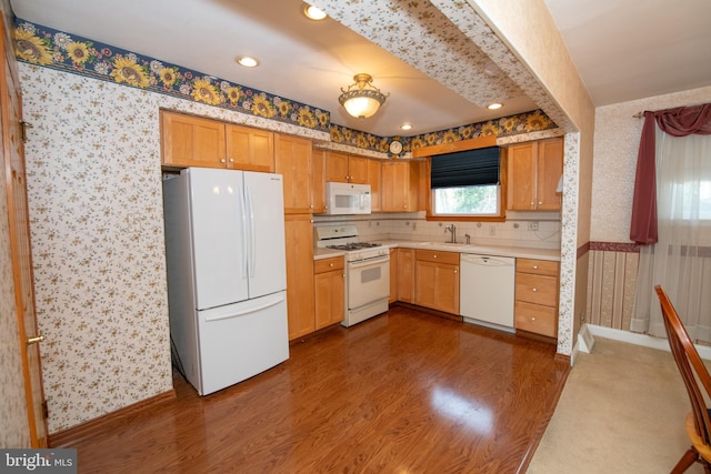 kitchen with dark wood-style floors, white appliances, wallpapered walls, and a sink