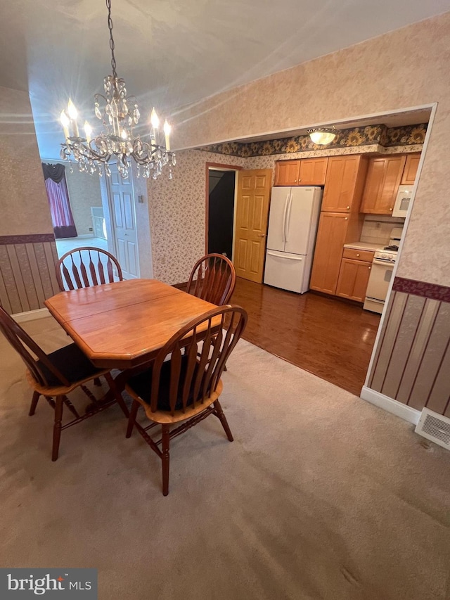 dining space with a notable chandelier, dark wood finished floors, wallpapered walls, dark colored carpet, and vaulted ceiling