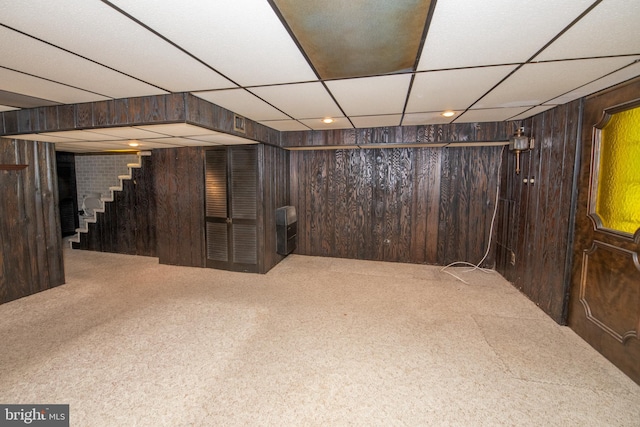 finished basement with stairway, a paneled ceiling, wooden walls, and carpet