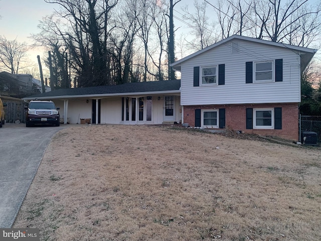 split level home with a front yard, brick siding, driveway, and fence