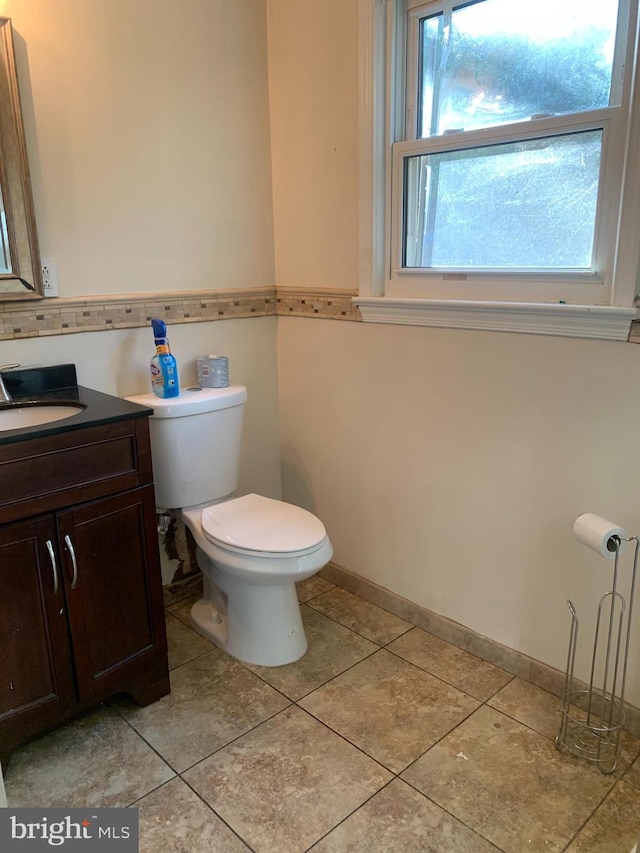 half bathroom featuring toilet, vanity, baseboards, and tile patterned floors